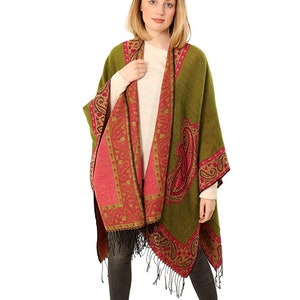 May include: A green and pink paisley patterned poncho with black fringe. The poncho is worn by a person with long blonde hair.