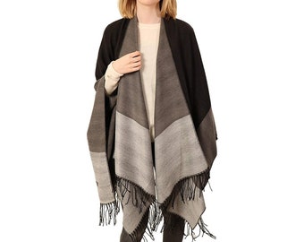 May include: A color-blocked poncho in shades of black, gray, and light gray. The poncho has a fringed hemline and is worn over a cream-colored top. The garment is designed with a geometric color-block pattern.