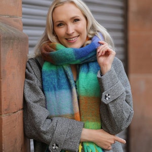 May include: A woman wearing a gray coat with a colorful striped scarf. The scarf has a fringe on the bottom and is tied around her neck.