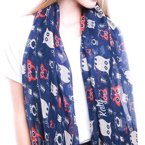 May include: A navy blue scarf featuring a repeating pattern of owls in red, white, and gray. The scarf has the name "Katy" printed on it. The scarf is draped over a white shirt.