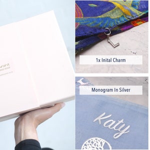 May include: A pink gift box with the text "Aurora Hand Made" on the top. The box is open and shows a variety of personalised gifts, including a scarf with a charm, a scarf with a birthstone, a scarf with a silver monogram, and a scarf with a gold monogram.