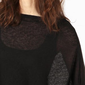 May include: Black sheer top with a scoop neck and long sleeves. The top is layered over a black tank top. The model has brown hair.