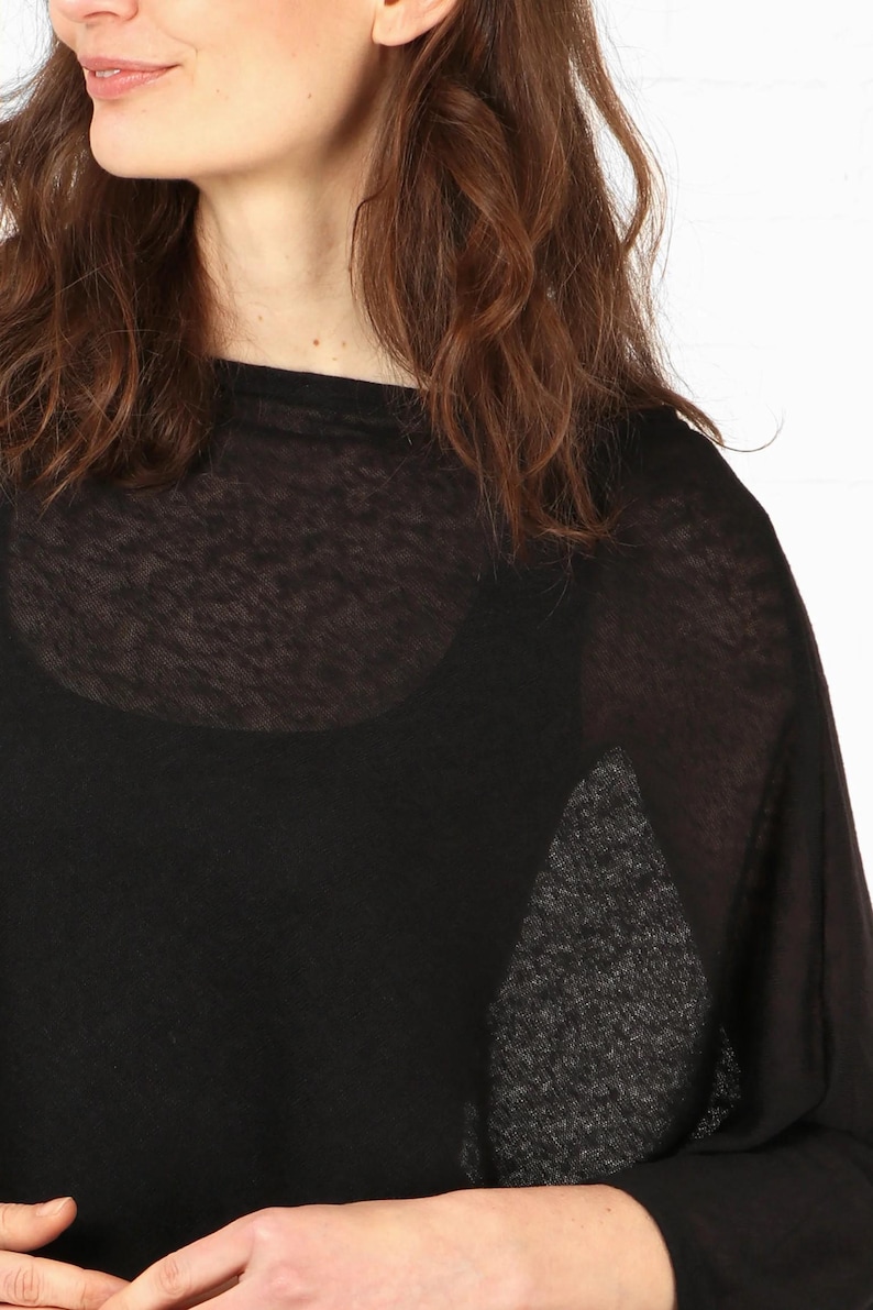 May include: Black sheer top with a scoop neck and long sleeves. The top is layered over a black tank top. The model has brown hair.