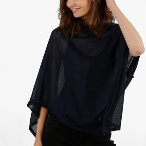 May include: Navy blue poncho-style top with a loose, flowing design. The top has a cowl neck and is made of a sheer, lightweight fabric. The garment is worn over a black top and paired with black pants.