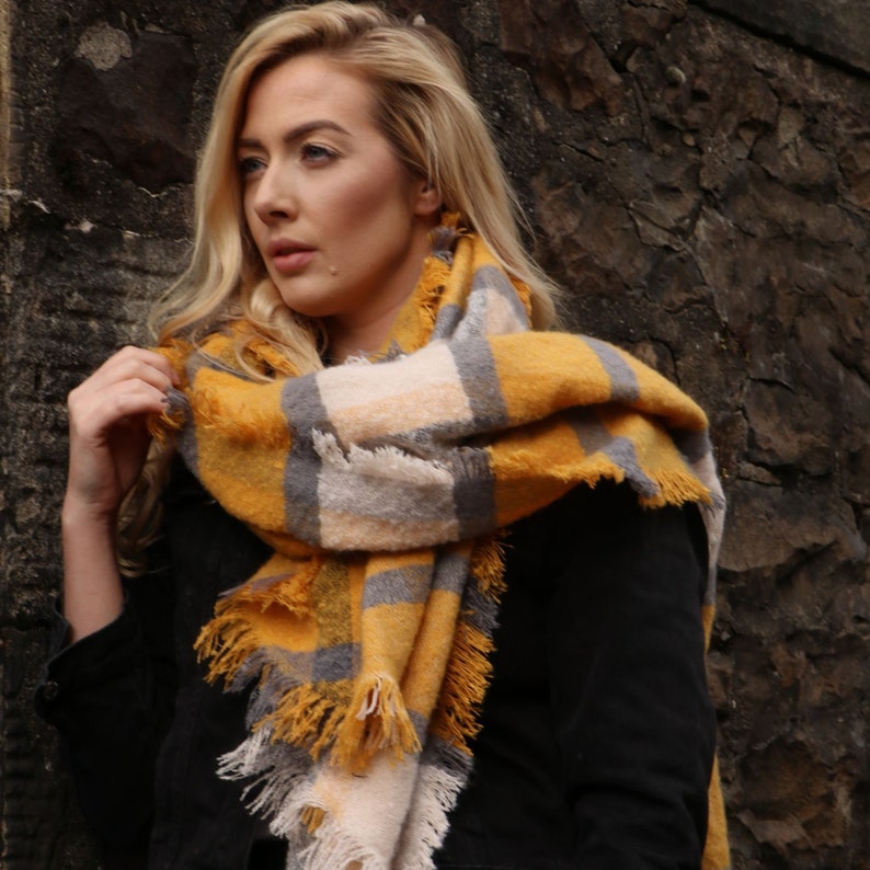 model wearing a mustard yellow plaid pattern winter blanket scarf around her neck and shoulders