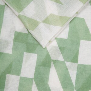 May include: White fabric with a green geometric pattern. The pattern is made up of overlapping squares and triangles.