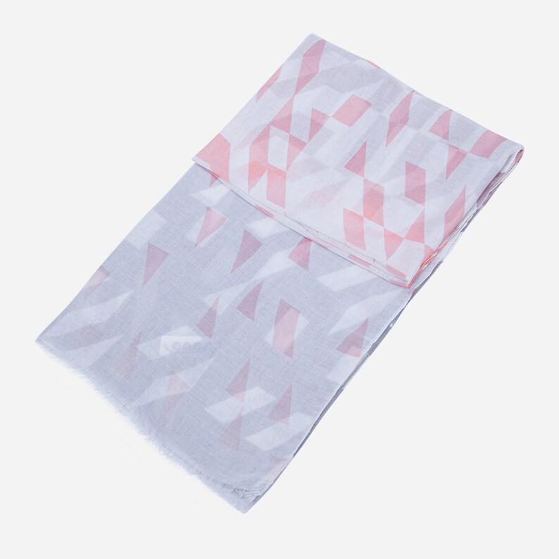 May include: A grey and pink patterned scarf with a geometric design. The scarf is folded in half and has a fringed edge.