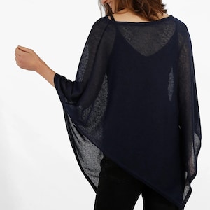 May include: Navy blue poncho-style top with a loose, flowing design. The top has a wide, boat-neck style neckline and short sleeves. The fabric appears lightweight and semi-sheer, suitable for layering. The model is wearing black pants.