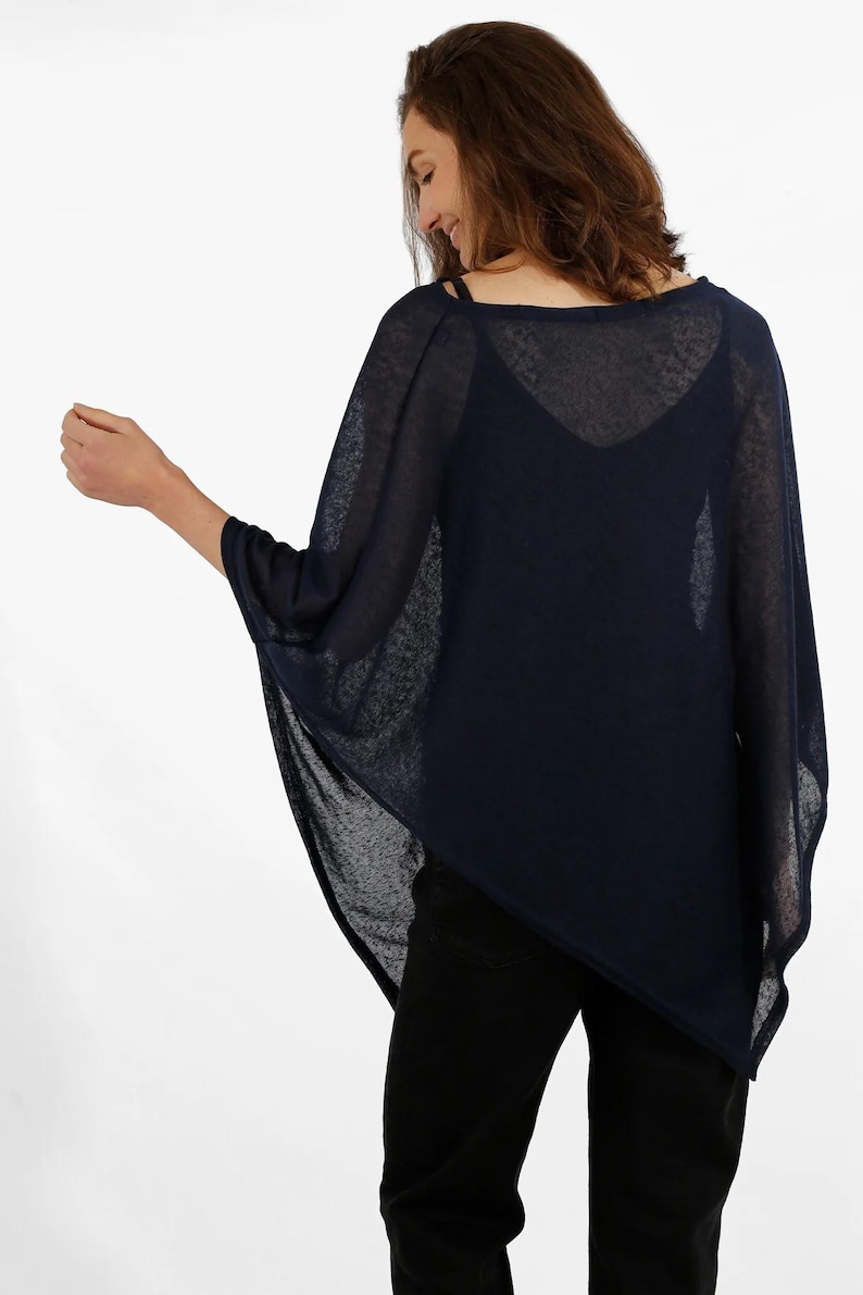 May include: Navy blue poncho-style top with a loose, flowing design. The top has a wide, boat-neck style neckline and short sleeves. The fabric appears lightweight and semi-sheer, suitable for layering. The model is wearing black pants.
