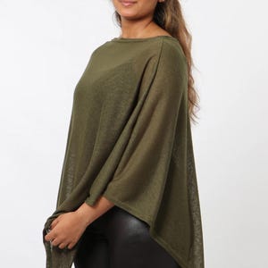 May include: Olive green poncho-style top with a loose, flowing design. The top has a boat neckline and a relaxed fit. The fabric appears lightweight and slightly sheer. The model is wearing black leggings. The background is plain white.