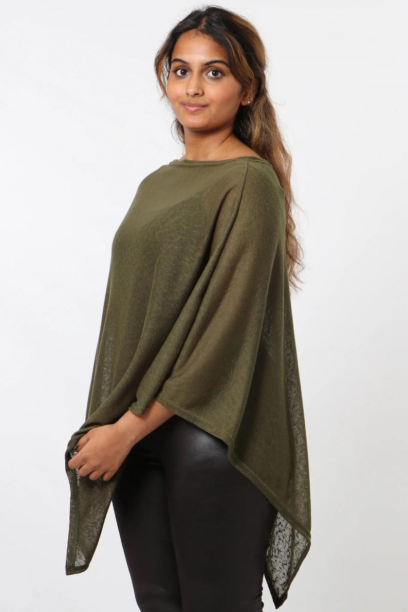 May include: Olive green poncho-style top with a loose, flowing design. The top has a boat neckline and a relaxed fit. The fabric appears lightweight and slightly sheer. The model is wearing black leggings. The background is plain white.