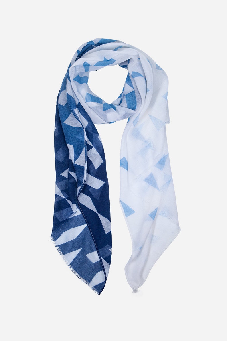 May include: A white and blue geometric patterned scarf with a fringed edge.