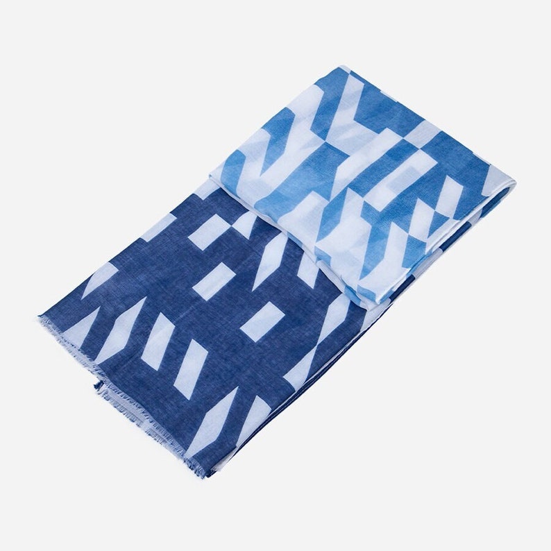 May include: A blue and white patterned scarf with a geometric design. The scarf is folded in half and has a fringed edge.