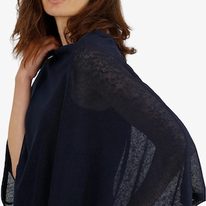 May include: A navy blue poncho-style top with a sheer, lightweight fabric. The garment has a loose, flowing design, with a draped appearance. The sleeves are wide and the fabric appears to be slightly textured. The top is a solid color and has a simple, elegant style.