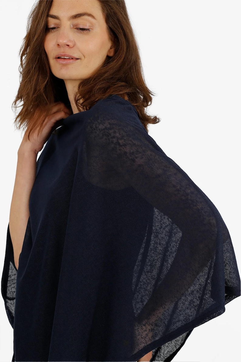 May include: A navy blue poncho-style top with a sheer, lightweight fabric. The garment has a loose, flowing design, with a draped appearance. The sleeves are wide and the fabric appears to be slightly textured. The top is a solid color and has a simple, elegant style.