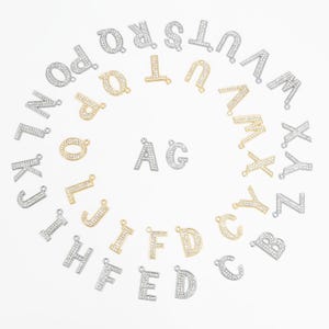 May include: A set of silver and gold letter charms with rhinestones. The letters are arranged in a circle, with the letter A and G in the center.