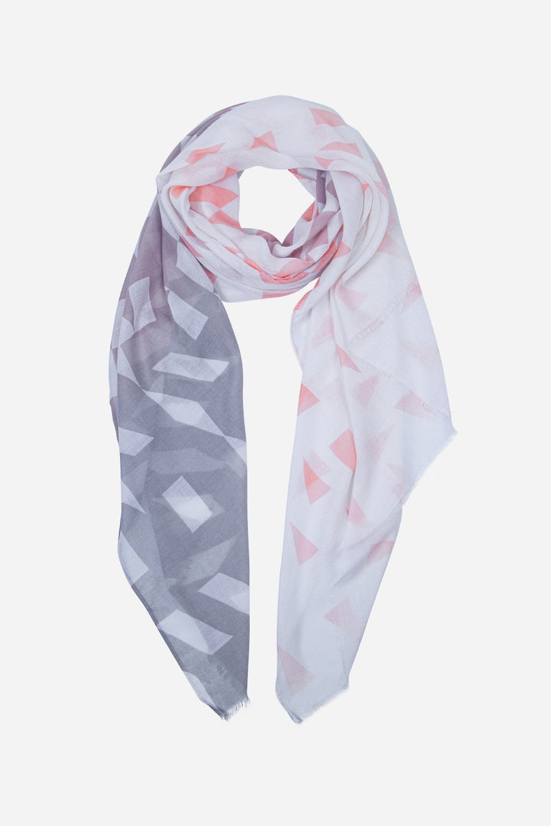 May include: A white and grey scarf with a geometric pattern. The pattern is made up of triangles and squares. The scarf is soft and lightweight.