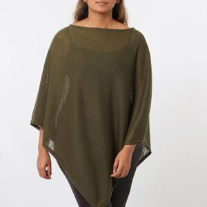 May include: An olive green poncho with a boat neck and asymmetrical hemline. The lightweight knitwear garment is worn over a black top and dark leggings. The poncho is a versatile piece of clothing.