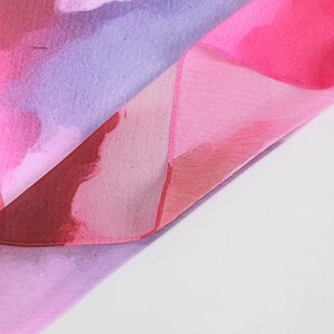 Pu&ograve; includere: Un tessuto rosa e viola con un design simile all'acquerello. Il tessuto &egrave; piegato a met&agrave;, mostrando i diversi colori e motivi.