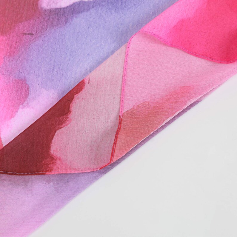 Pu&ograve; includere: Un tessuto rosa e viola con un design simile all'acquerello. Il tessuto &egrave; piegato a met&agrave;, mostrando i diversi colori e motivi.