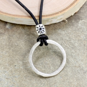 May include: A silver circle pendant necklace with a black leather cord. The pendant has a hammered texture and is attached to the cord with a silver bead featuring a starburst design.
