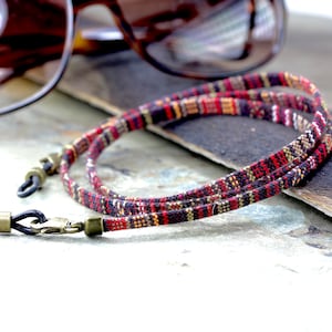 May include: A red, black, and gold patterned eyeglass chain with black rubber ends and antique gold metal clasps.