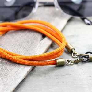 May include: Orange and black eyeglass strap with metal clasps. The strap is made of a braided cord and is designed to hold glasses securely around the neck.
