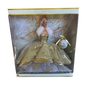 May include: A Barbie doll in a box, the Special 2000 Edition. The doll wears a gold gown with a white fur stole and a crown. She holds a Christmas ornament. The box has the words "Celebration Barbie".