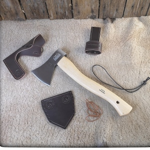 May include: A small axe with a wooden handle and a brown leather sheath. The axe has a black blade with a U.S.A. Hickory label on the handle. The sheath has a brown leather strap with a metal buckle.