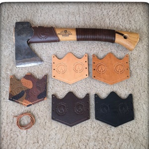 May include: Five leather axe sheaths, two in brown, two in black, and one in camouflage. The sheaths have the text "Prometheus Hels" and a flame logo. A small brown leather cord is also pictured.
