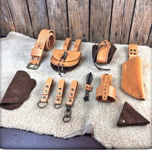 May include: A set of leather goods including a belt, a pouch, a small bag, a key chain, and a coin purse. The items are all made of brown leather and have a rustic, handmade look.