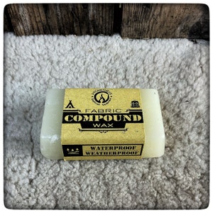 Pode incluir: Uma barra de cera composta para tecido bege com um rótulo castanho que diz "Prometheus Outdoor Equipment", "Fabric Compound Wax" e "Waterproof Weatherproof".
