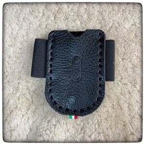 May include: Black leather card holder with a stitched edge and elastic wrist strap. The holder has a logo embossed on the front.