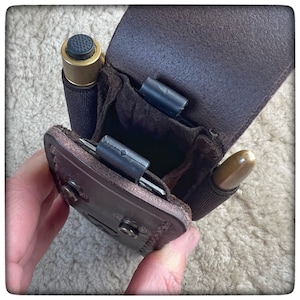 May include: A brown leather pouch with two compartments, one for a small brass tool and the other for a wooden tool. The pouch has a snap closure and is designed to be worn on a belt.