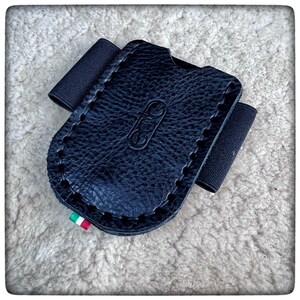 May include: Black leather card holder with a black elastic band and a stitched edge. The holder has a small Italian flag sewn on the bottom.