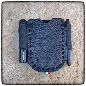 May include: Black leather case with two black tools, one with the word "OLIGHT" printed on it. The case has a stitched edge and a small Italian flag.