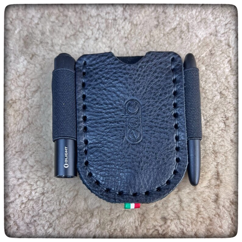 May include: Black leather case with two black tools, one with the word "OLIGHT" printed on it. The case has a stitched edge and a small Italian flag.