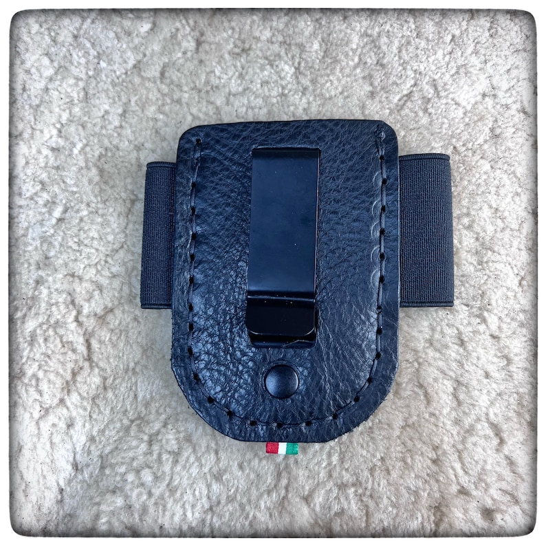 May include: Black leather phone case with a belt clip and elastic band. The case has a textured surface and a stitched edge.