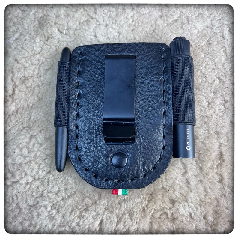 May include: Black leather carrying case with a belt clip, designed to hold a pen and a torch. The torch has the brand name "Olight" printed on the side.