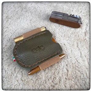 May include: A green leather wallet with a brown strap and a brass buckle. The wallet has the word "ede" embossed on the front.