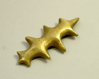 May include: A gold-colored metal brooch with a jagged, star-shaped design.