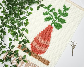 May include: A white crocheted wall hanging with a fringe border features a green plant in a peach-colored vase. The vase has white stripes and is sitting on a brown crocheted base.