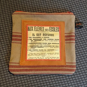 May include: A brown and tan striped fabric pouch with a zipper closure. The pouch has a leather patch with a vintage-style sign that reads "Aux Eleves des Ecoles Il Est Defendu" and lists a series of rules in French.