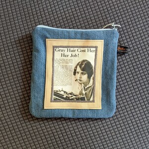 Puede incluir: Una bolsa de cremallera de mezclilla azul con un anuncio vintage de tinte para el cabello. El anuncio presenta a una mujer con una m&aacute;quina de escribir y el texto "Gray Hair Cost Her Her Job!"