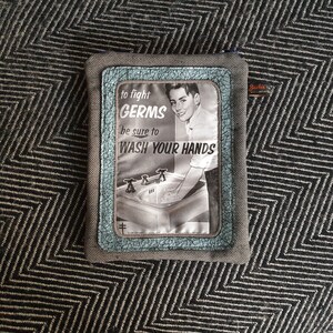 May include: A gray fabric pouch with a blue and white patch featuring a vintage illustration of a boy washing his hands at a sink. The patch has the text "to fight GERMS be sure to WASH YOUR HANDS".