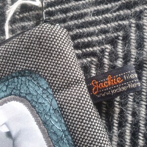 May include: A black and white checkered fabric zippered pouch with a blue and green leather patch and a black label with the text "Jackie file" and "www.jackie-file.v" in orange.