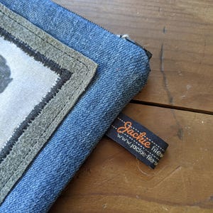 May include: A blue denim zippered pouch with a gray fabric patch and a black label that reads "Jackie fileu www.jackie-fileu.com".