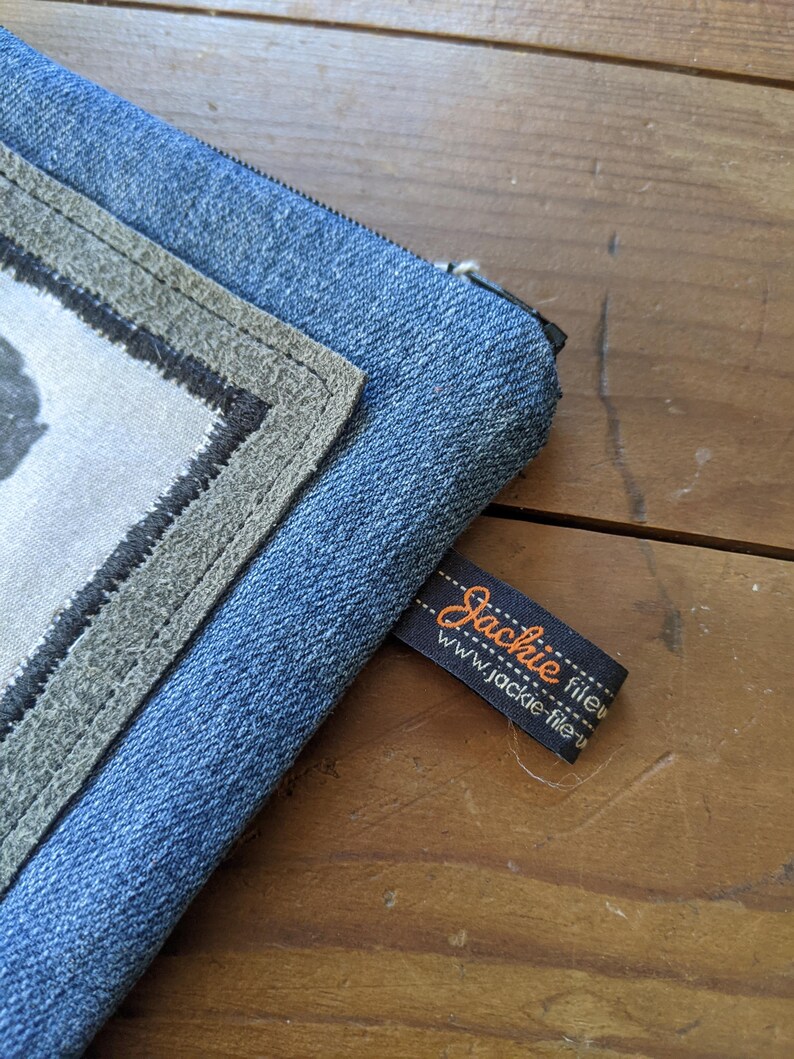 May include: A blue denim zippered pouch with a gray fabric patch and a black label that reads "Jackie fileu www.jackie-fileu.com".