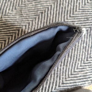 May include: Close-up of a black zipper on a navy blue pouch. The zipper is open, revealing the inside of the pouch.