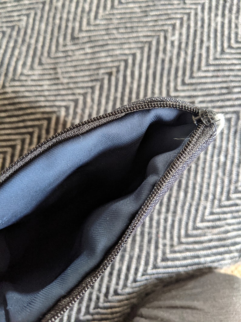 May include: Close-up of a black zipper on a navy blue pouch. The zipper is open, revealing the inside of the pouch.